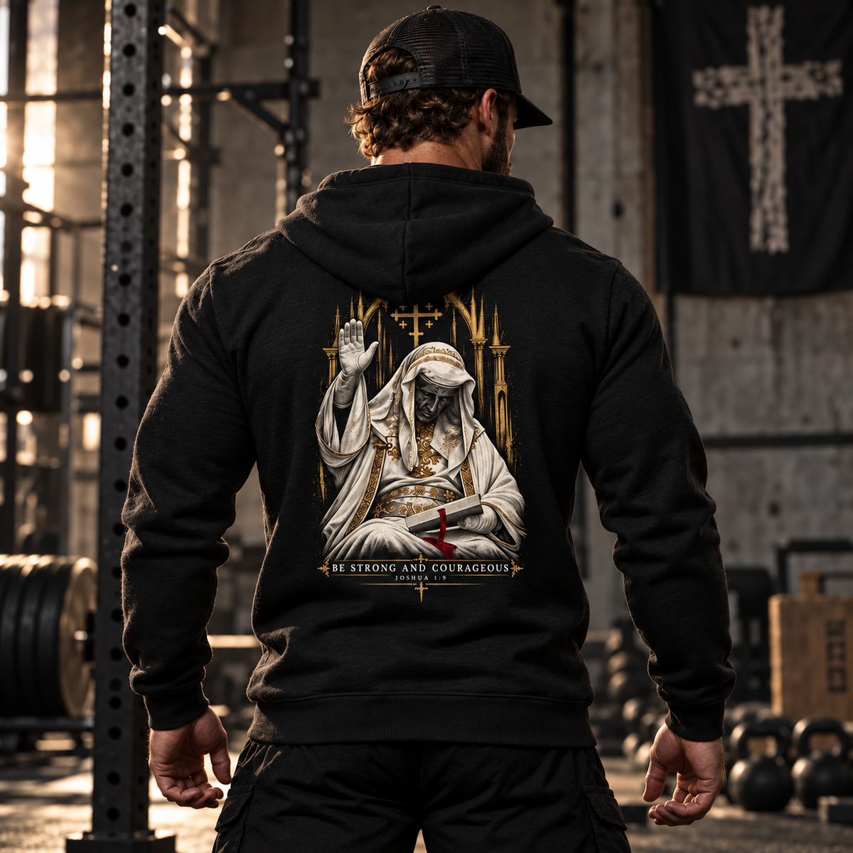 Man in a gym wearing the Built Daily King Baldwin hoodie, back view: BE STRONG AND COURAGEOUS
